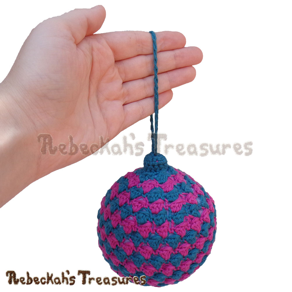 Striped Bobble Bauble hanging on my hand! | Amigurumi Crochet Pattern by @beckastreasures | Written pattern + photo tutorials too | Available to purchase in my #Ravelry & Website shops or via #GreybriarsTravels magazine - Get your copy today! | #crochet #pattern #amigurumi #christmas #bauble #ornament 